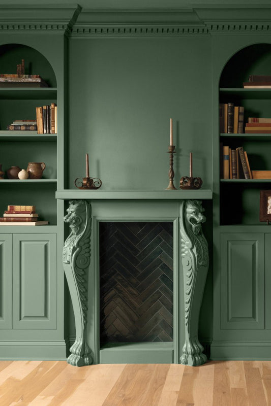 A green painted room with lower panelled walls and arched, built-in shelving topped with books and decor.